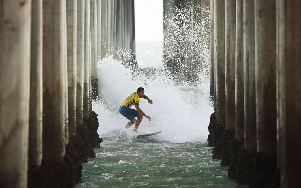 Il brasiliano Ian Gouvela surfa tra i piloni del molo ad Huntington Beach, in California (Afp)